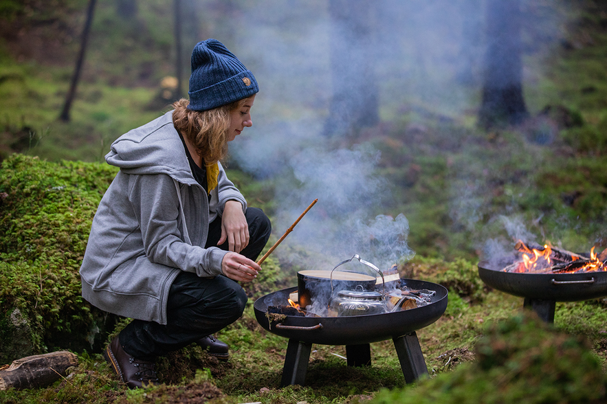 A girl wearing a hat cooking over open fire in the forest